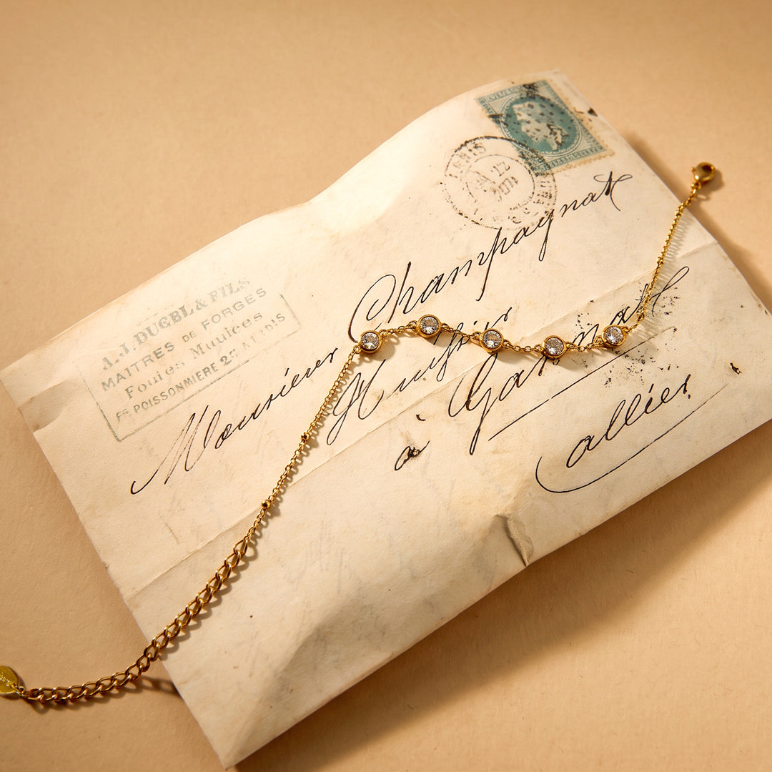 Gold geometric charm bracelet with clear stones on an antique envelope.