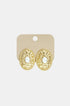 Gold oval stud earrings with a hammered texture and a pearl in the center, on a light beige card.