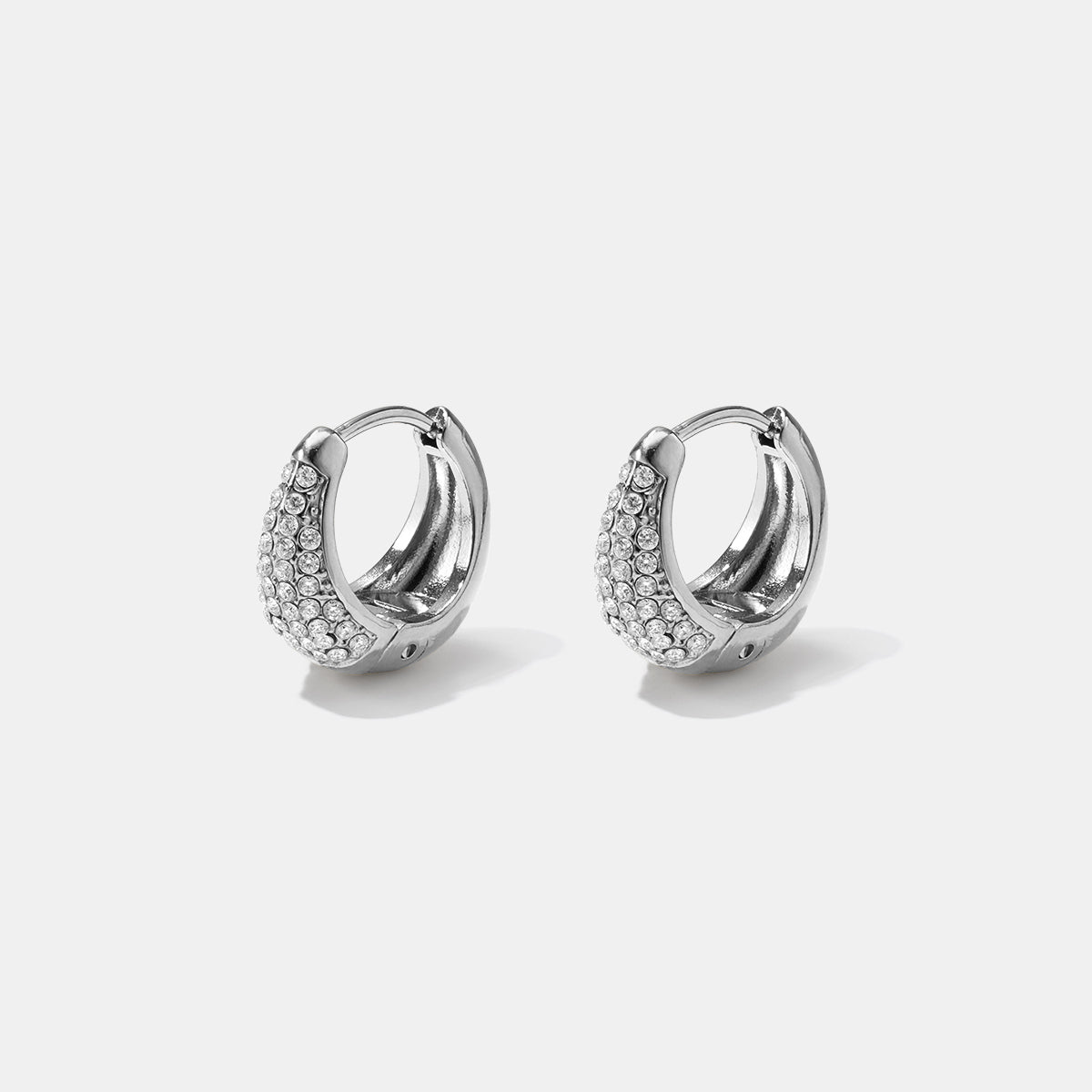 Silver hoop earrings with a curved design encrusted with small clear rhinestones.