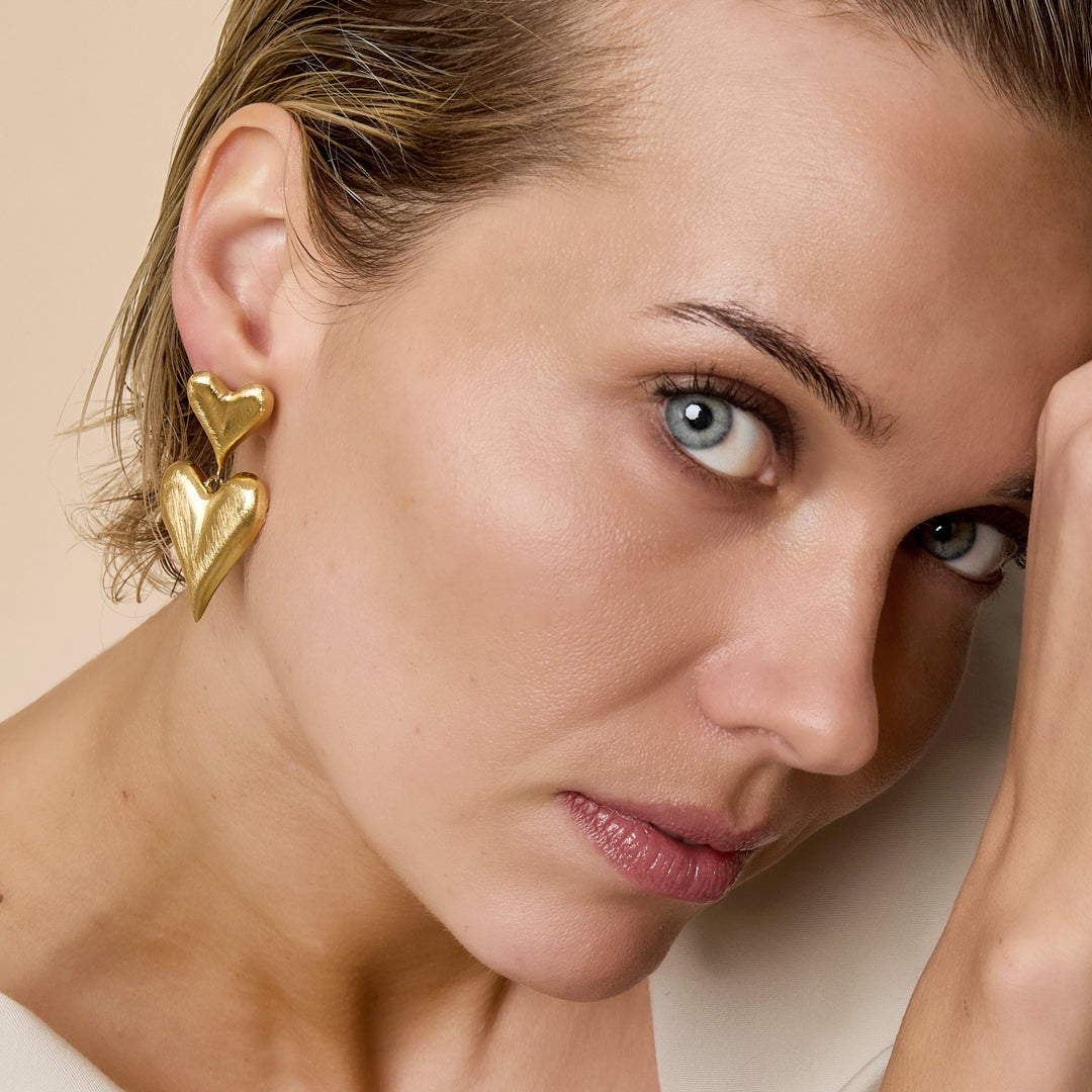 Gold heart drop earrings with a smaller heart above a larger heart.