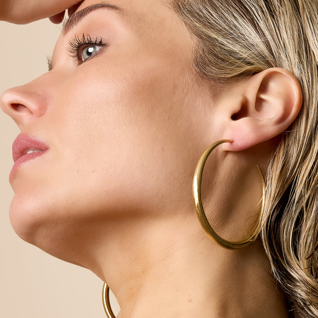Gold hoop earrings worn by a woman, showing the detail of the jewelry.