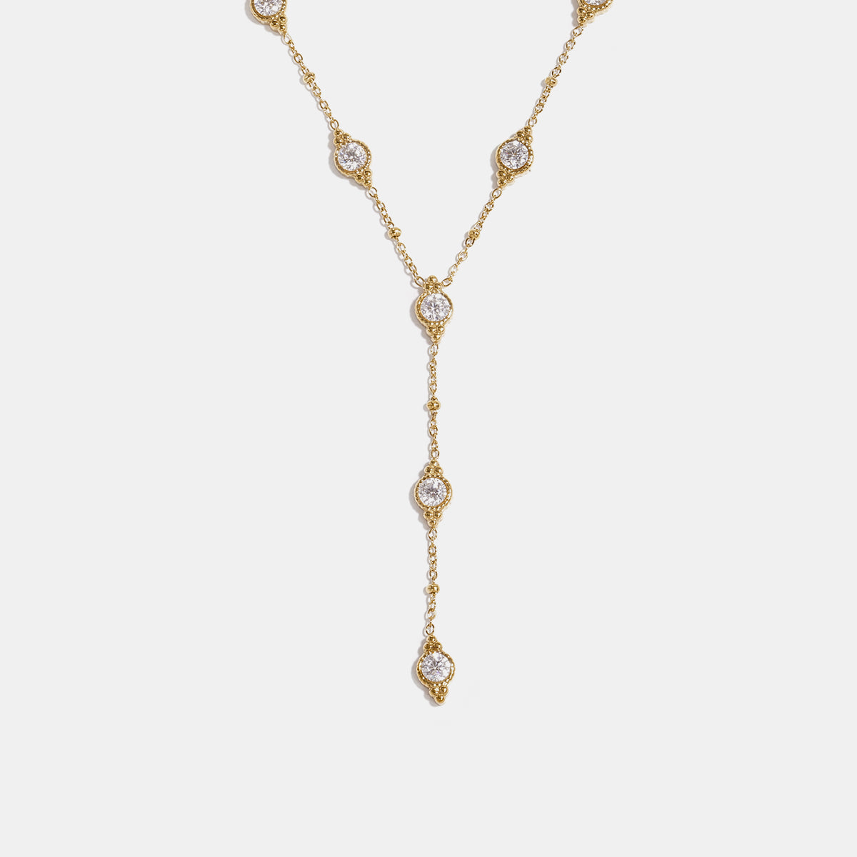 Gold Y-shaped necklace with a chain of small beads and circular pendants, each with a clear stone.