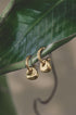Gold-colored, matte finish Sierra drop earrings with sculptural, irregular shapes hanging from a green leaf.
