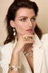 Gold dangle earrings with shell and pearl accents, worn by a model.