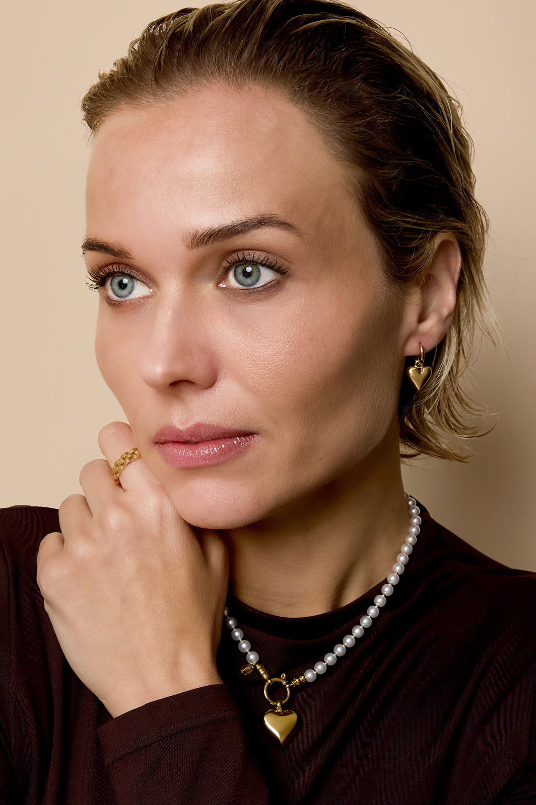 Gold heart drop earrings on a woman wearing a pearl necklace and a gold ring.