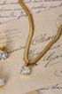 Gold snake chain necklace with a cushion-cut clear stone pendant, resting on vintage paper.