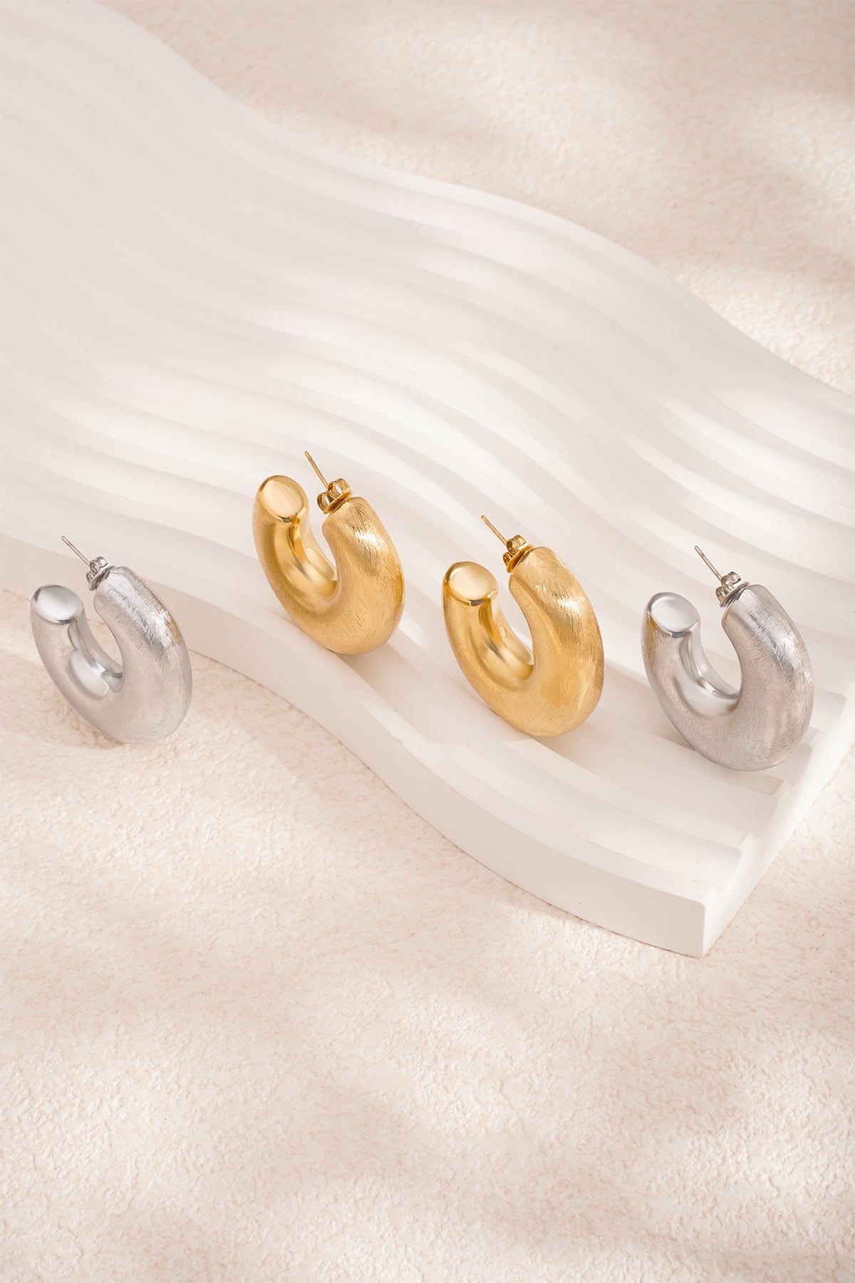 Two pairs of Elysian Hoop Earrings, one gold and one silver, with a brushed finish.