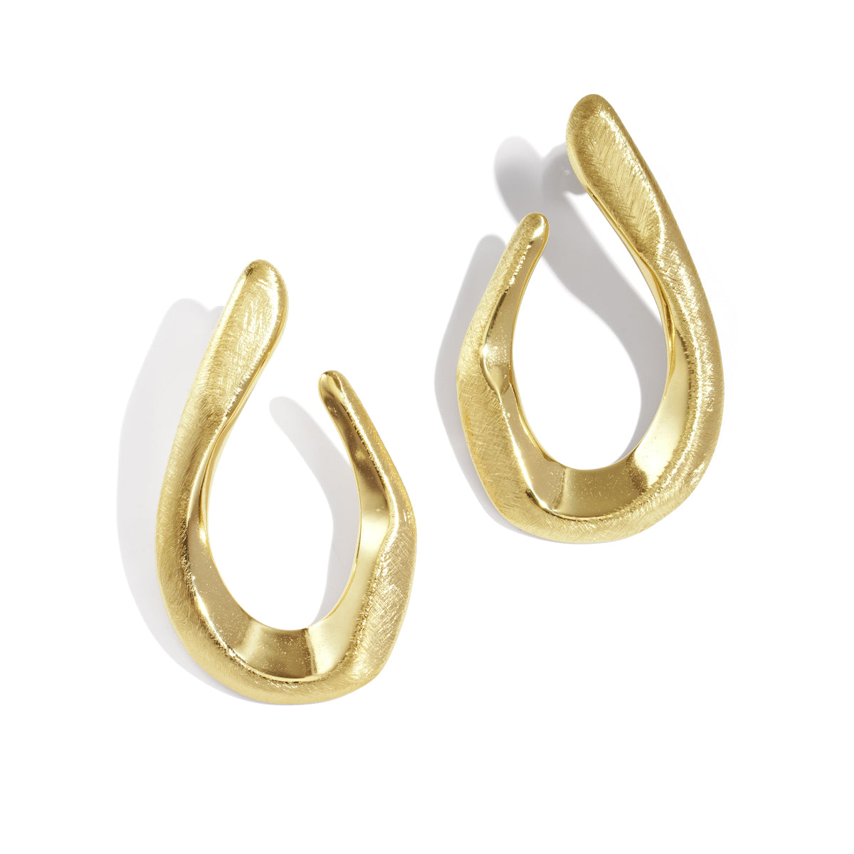 Two irregular shaped gold stud earrings with a brushed finish, casting shadows on a white background.
