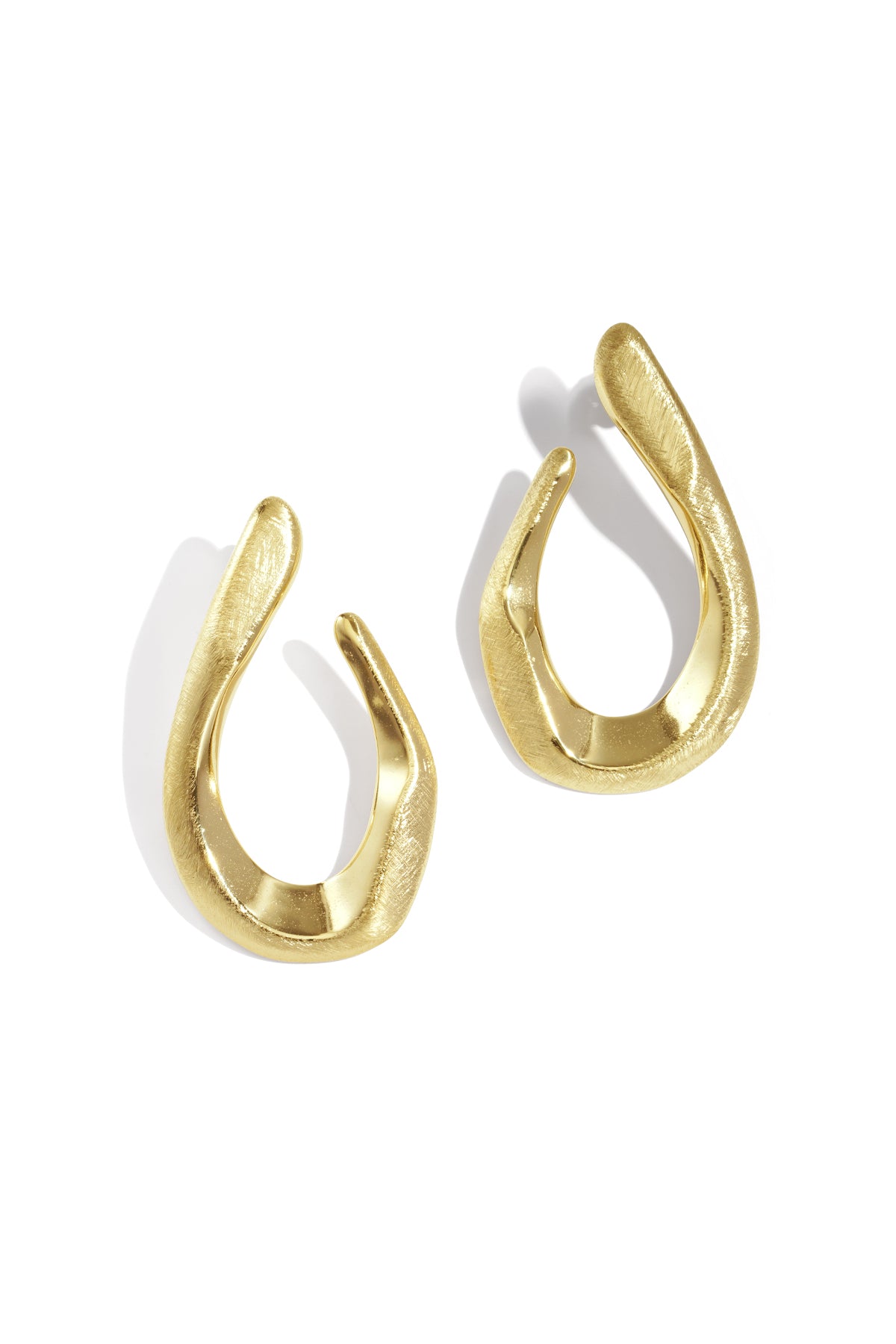 Two irregular shaped gold stud earrings with a brushed finish, casting shadows on a white background.