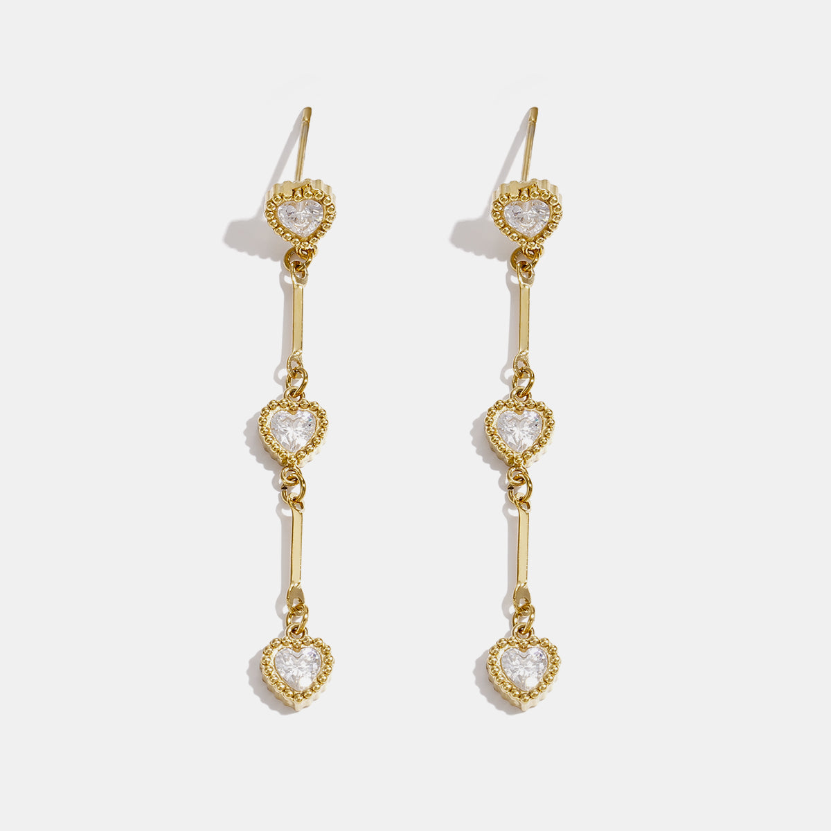 Gold dangle earrings with three heart-shaped zircon charms hanging from a bar.