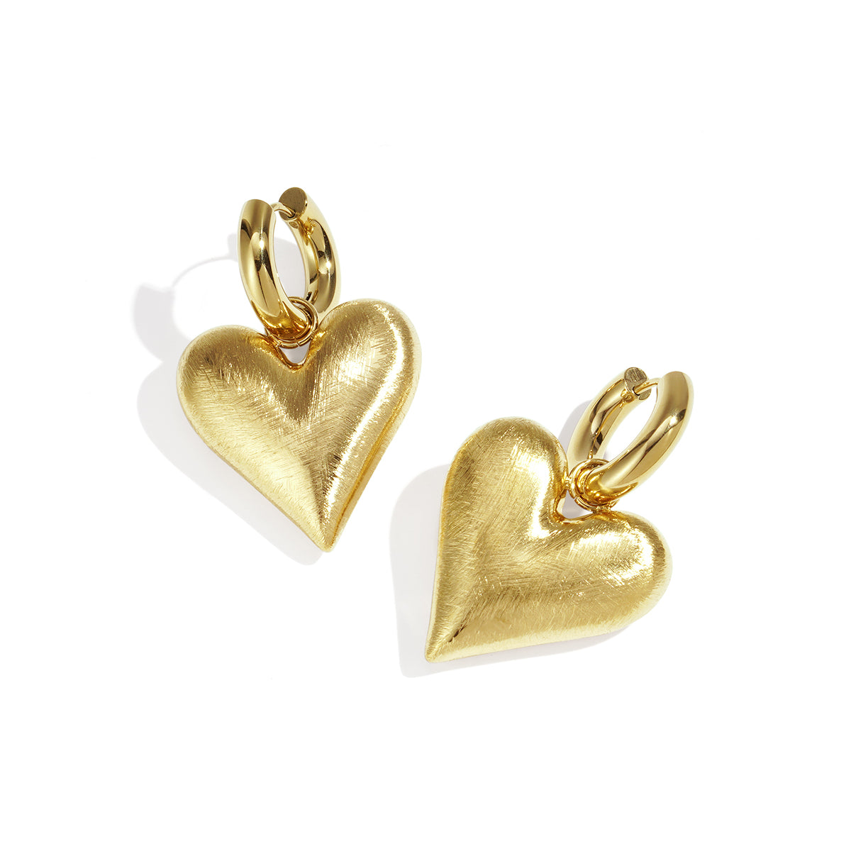 Gold heart drop earrings with a brushed finish, attached to gold hoops.