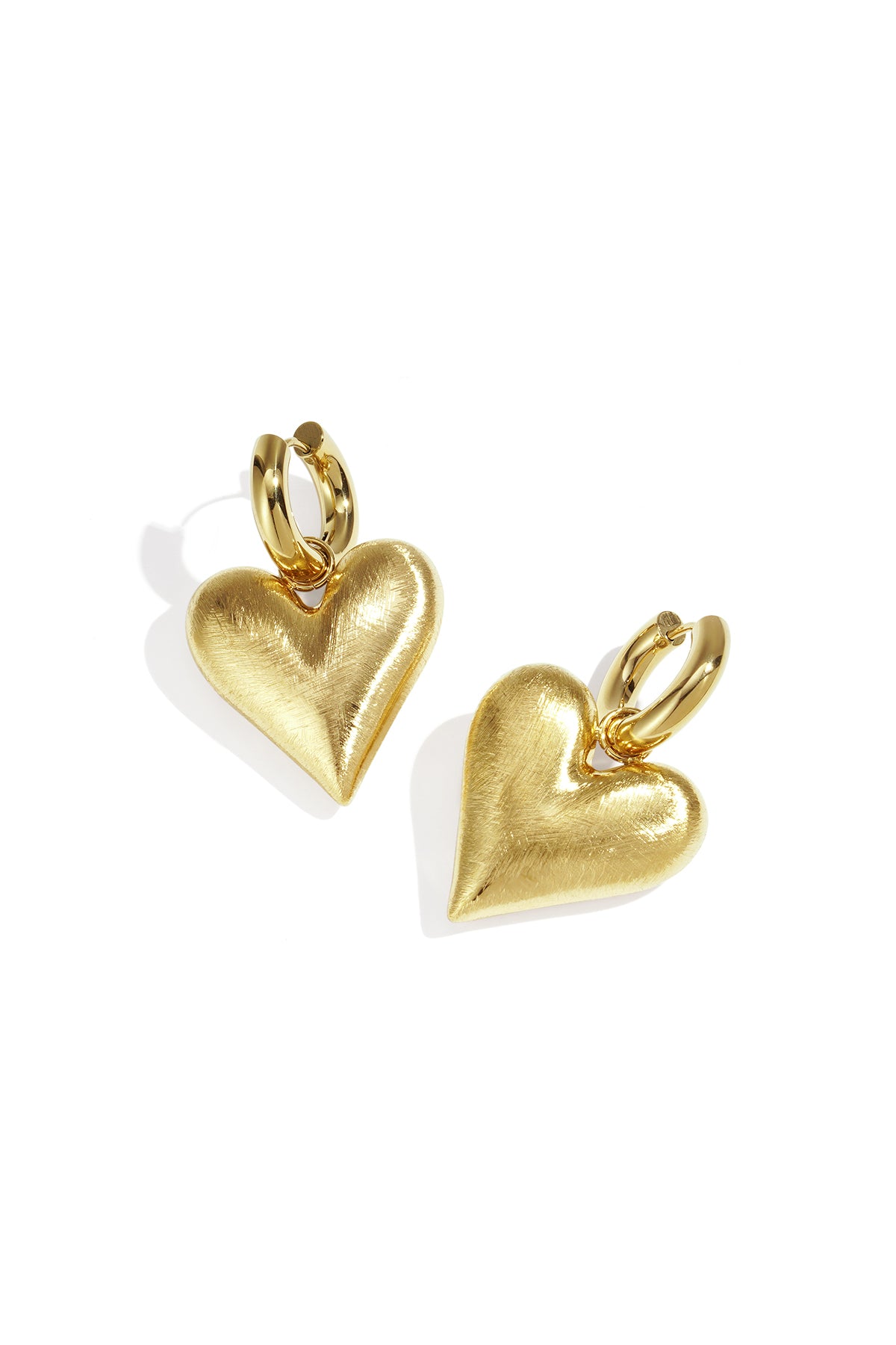 Gold heart drop earrings with a brushed finish, attached to gold hoops.