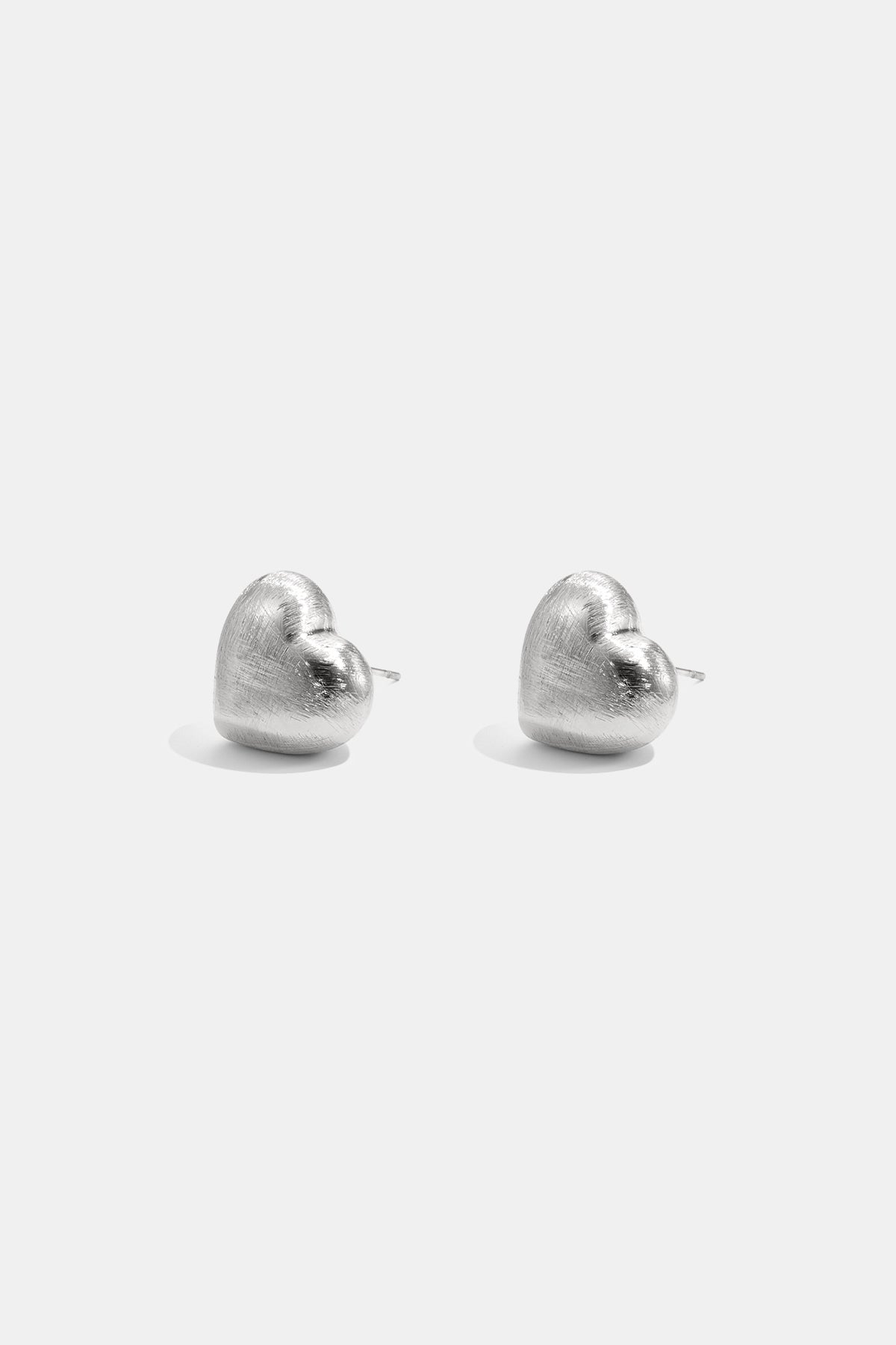 Two silver heart-shaped stud earrings with a matte finish, displayed against a white background.