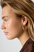 Gold Aurelia hoop earrings with a textured surface, worn by a woman.