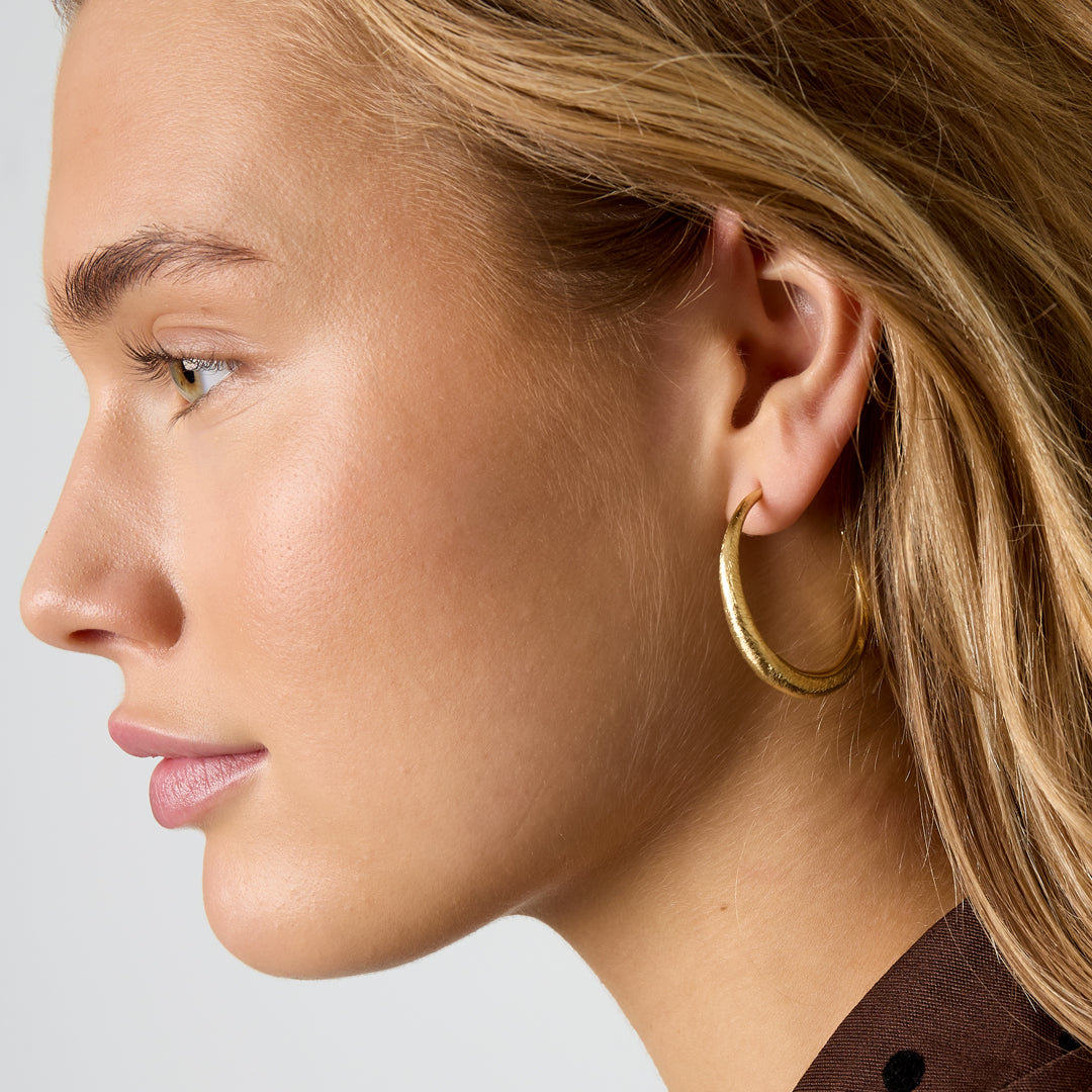 Gold Aurelia hoop earrings with a textured surface, worn by a woman.