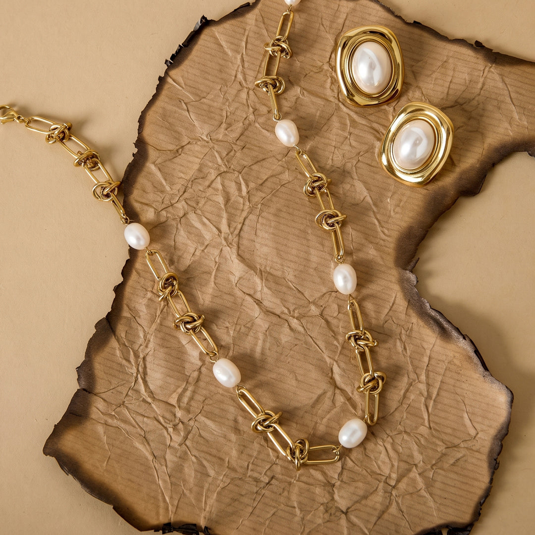 Gold chain necklace with pearls and matching oval pearl earrings on burnt paper.