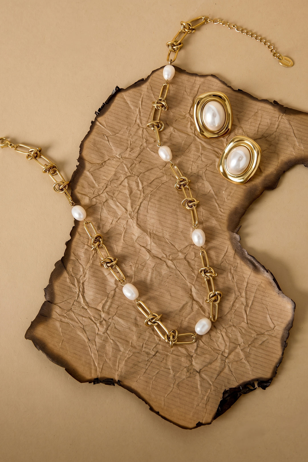 Gold chain necklace with pearls and matching oval pearl earrings on burnt paper.