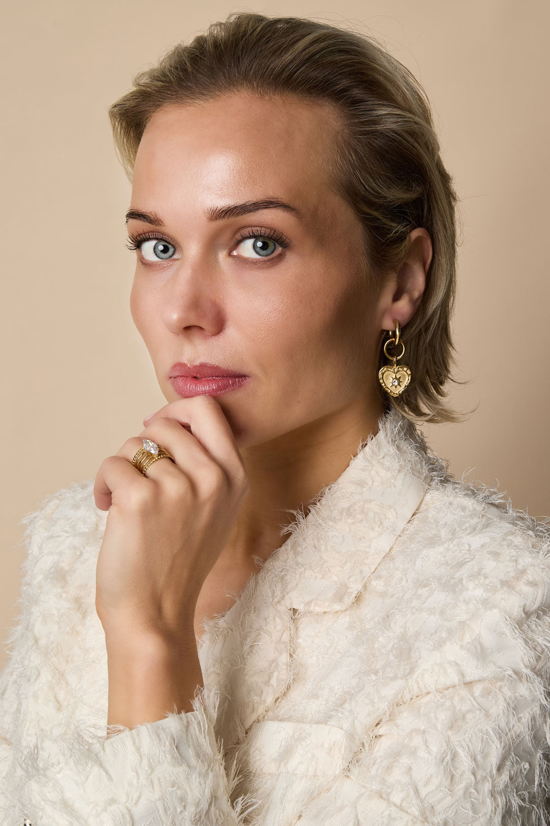 Gold heart drop earrings with rhinestones and a diamond ring on a woman's hand.