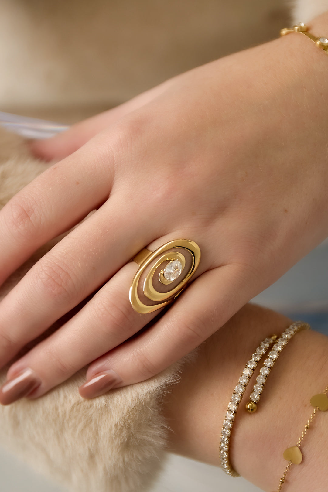 Gold ring with intertwined spiral design and a central zircon stone, worn on a finger.