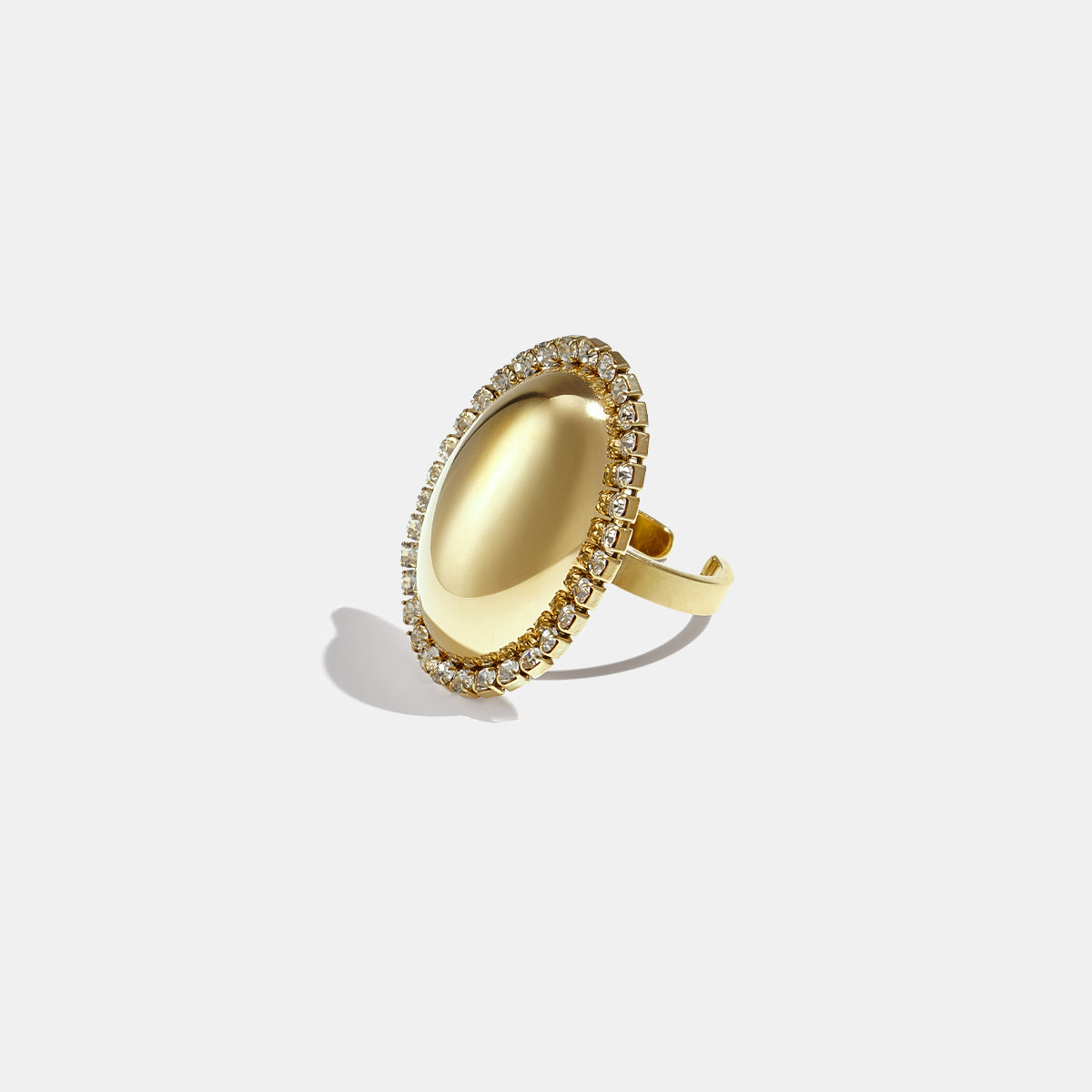 Gold-toned oval statement ring with a smooth, reflective surface surrounded by a halo of clear rhinestones.