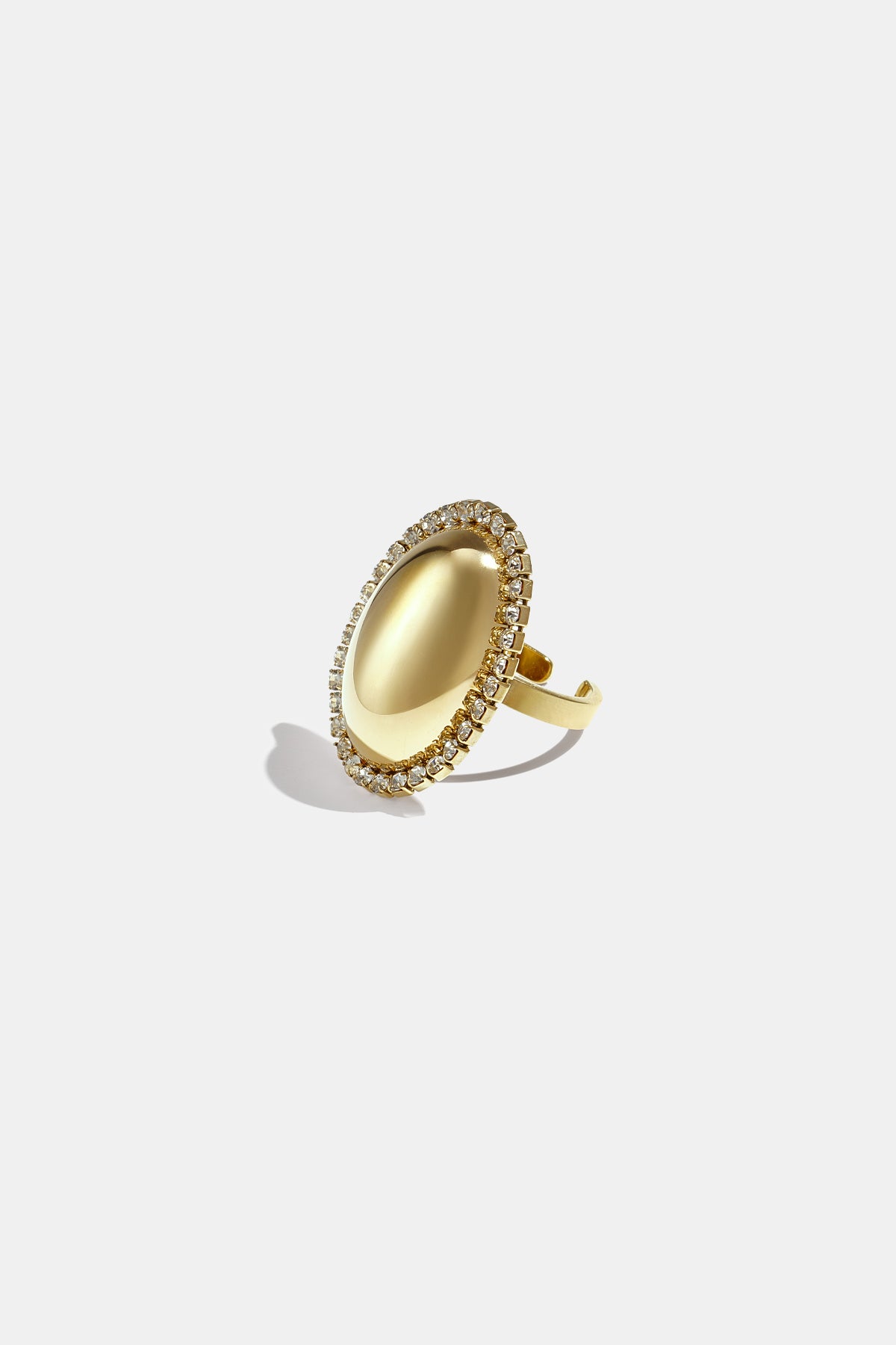 Gold-toned oval statement ring with a smooth, reflective surface surrounded by a halo of clear rhinestones.