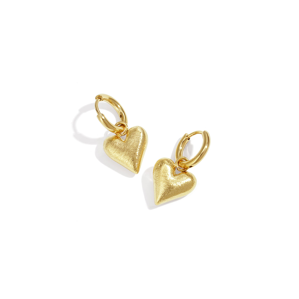 Gold heart drop earrings with a brushed finish, casting a shadow on a white background.