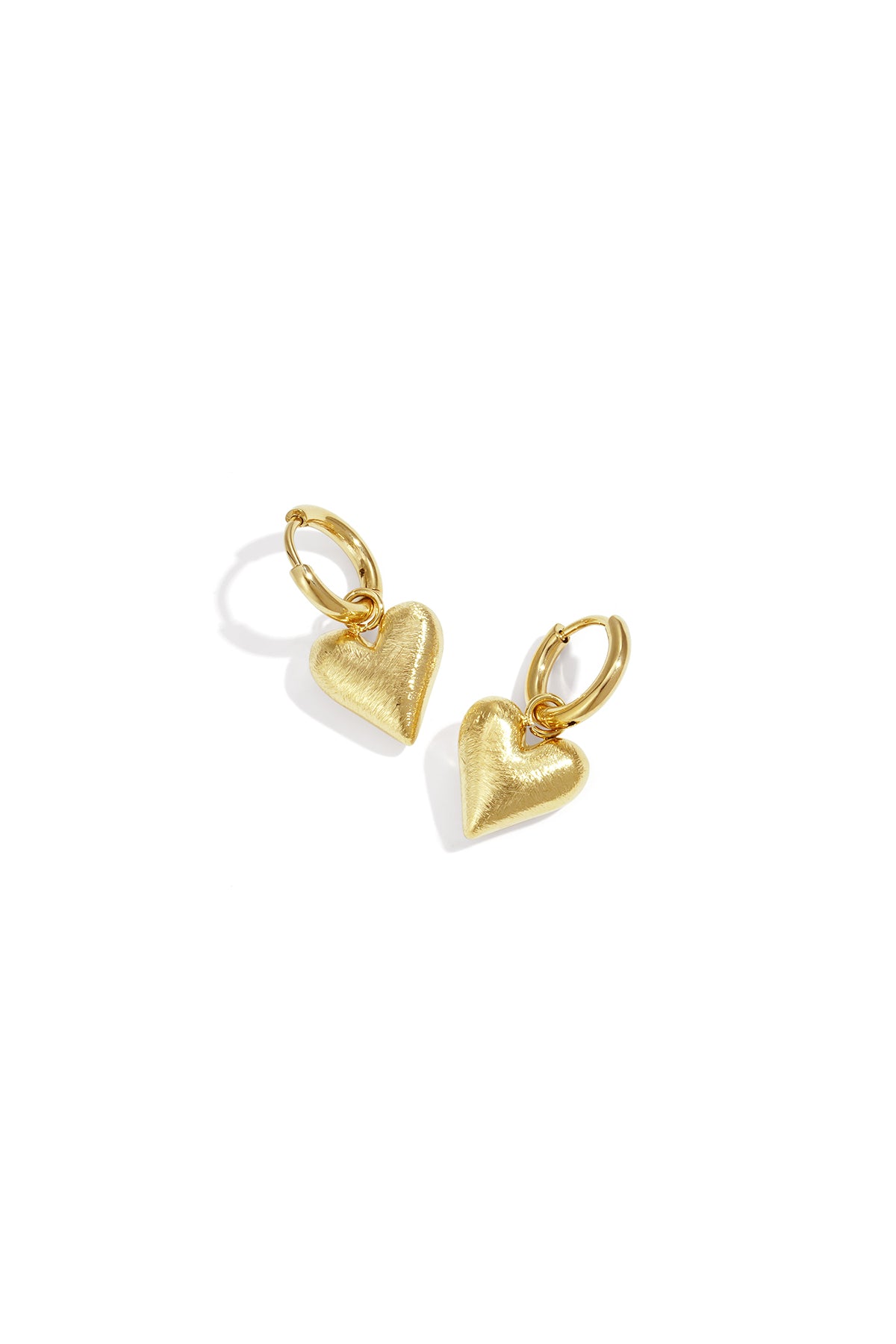 Gold heart drop earrings with a brushed finish, casting a shadow on a white background.