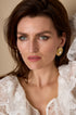 Gold Aurelia stud earrings with pearl detail worn by a woman with blue eyes and brown hair.