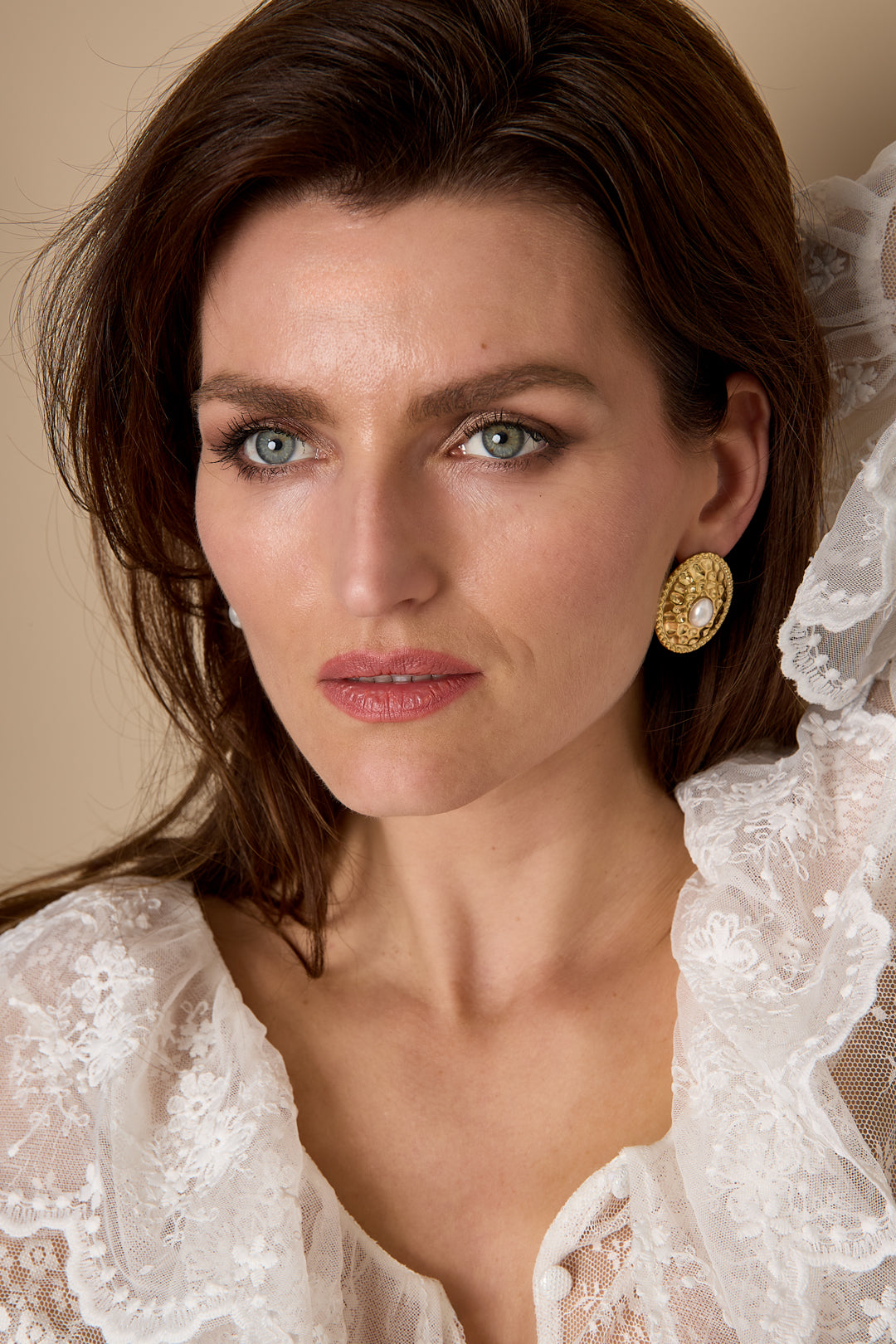 Gold Aurelia stud earrings with pearl detail worn by a woman with blue eyes and brown hair.