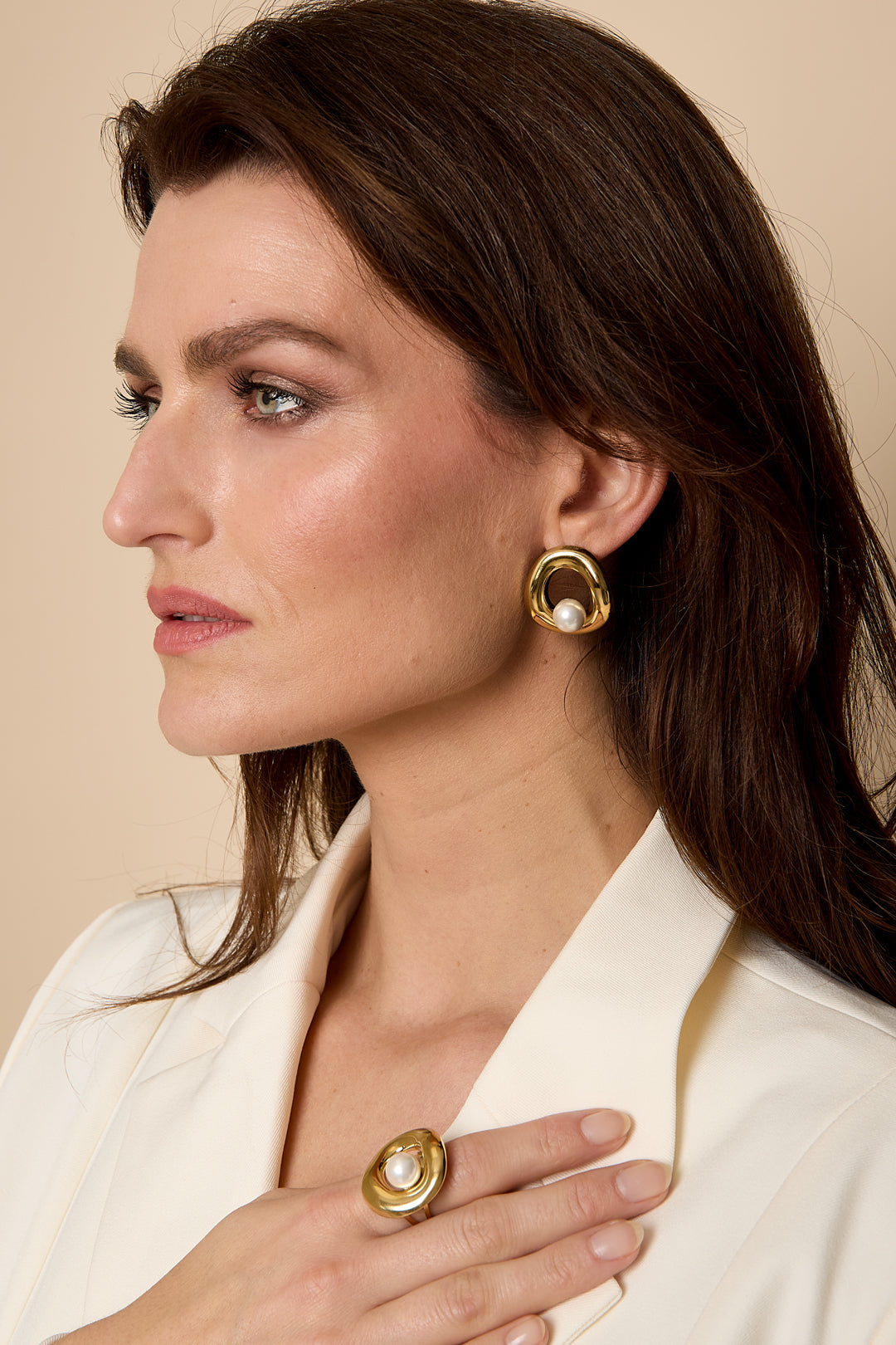Gold circle stud earrings with a pearl accent, worn by a woman.