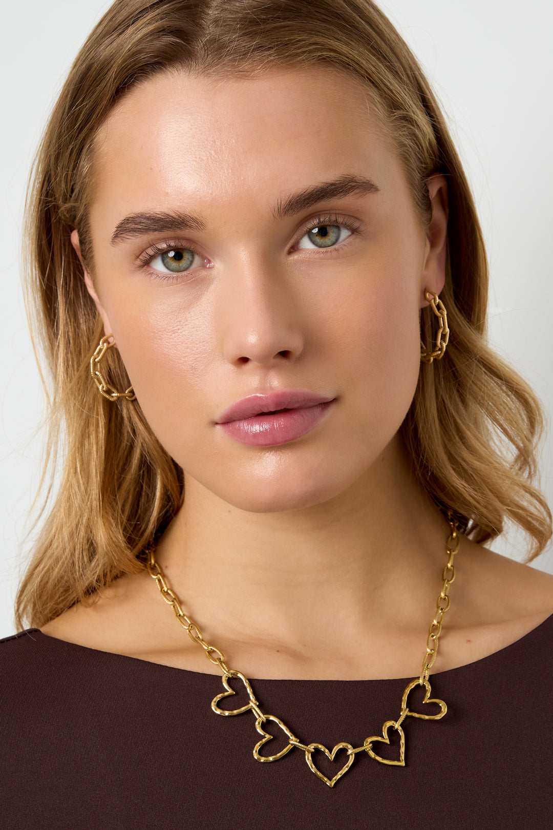 Gold chain necklace with heart pendants and gold hoop earrings on a woman