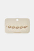 Gold geometric charm bracelet with five clear stones on a beige card.