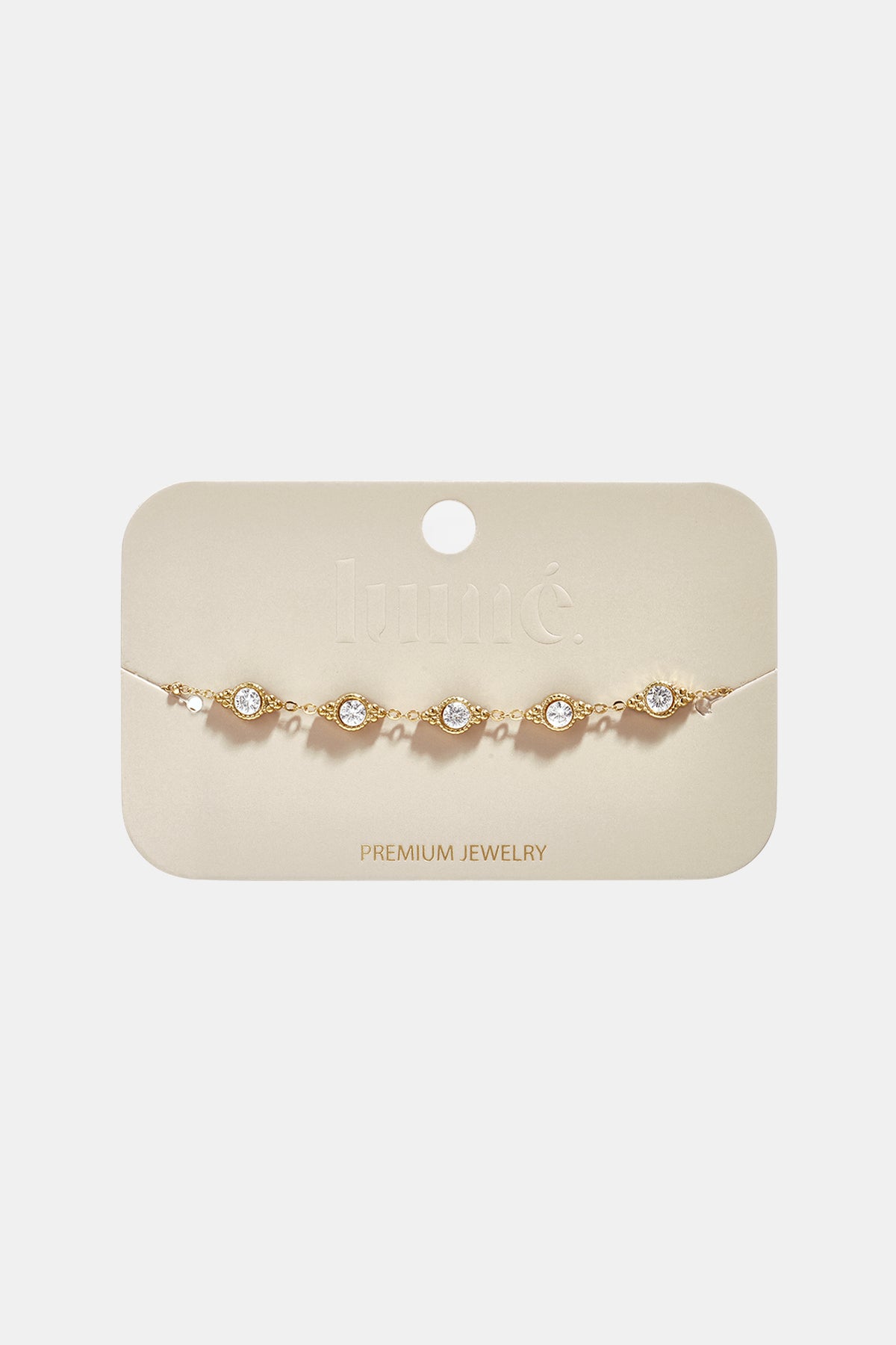 Gold geometric charm bracelet with five clear stones on a beige card.