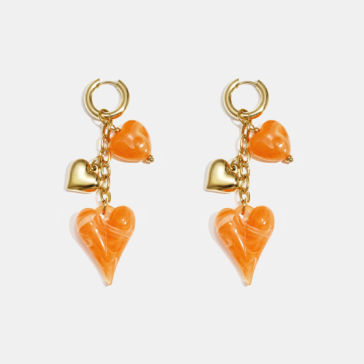 Gold hoop earrings with dangling orange acrylic hearts and gold heart charms.