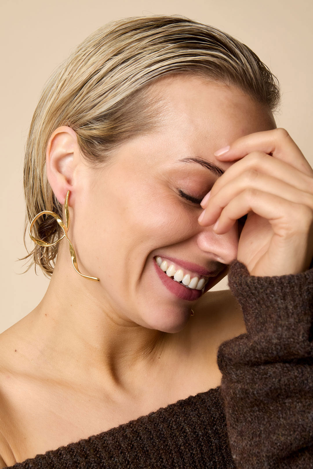Gold-toned abstract bow-shaped earrings on a woman laughing.