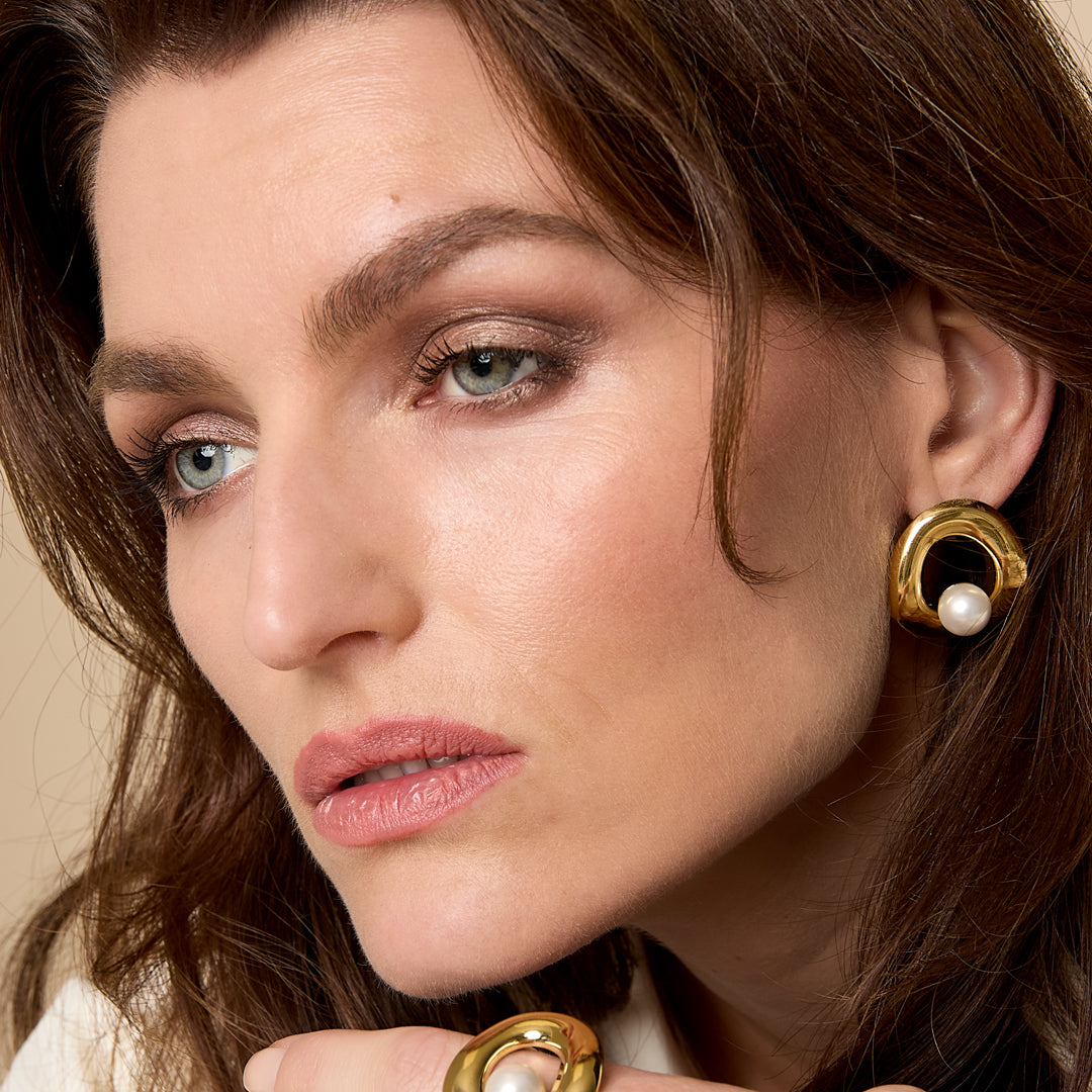 Gold circle stud earrings with a pearl accent, worn by a woman.