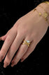 Gold adjustable ring with a clear oval stone on a hand with brown nails and a gold bracelet.