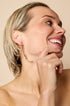 Gold-toned abstract sculptural earrings on a woman's ear.