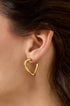 Gold heart hoop earring on a person's ear.