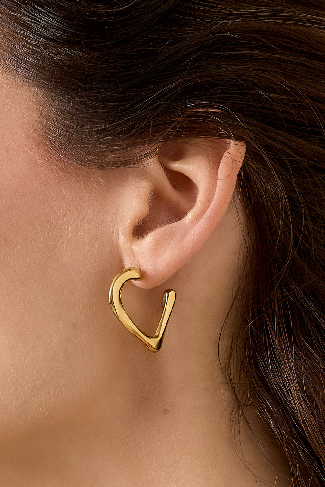 Gold heart hoop earring on a person's ear.