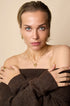 Gold heart pendant necklace on a woman wearing a brown off-the-shoulder sweater.