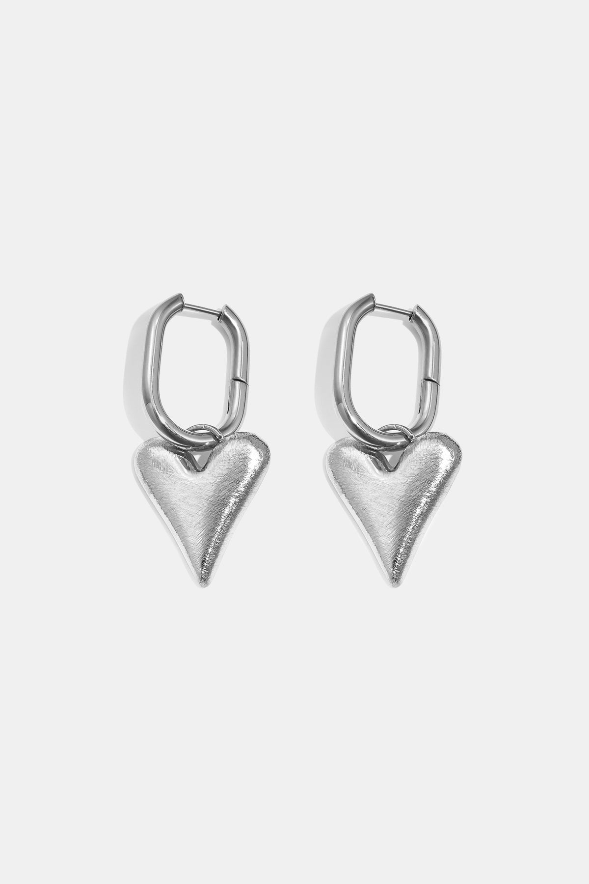 Silver heart drop earrings with oval hoops, against a white background.