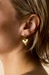 Gold heart drop earring on a person's ear.
