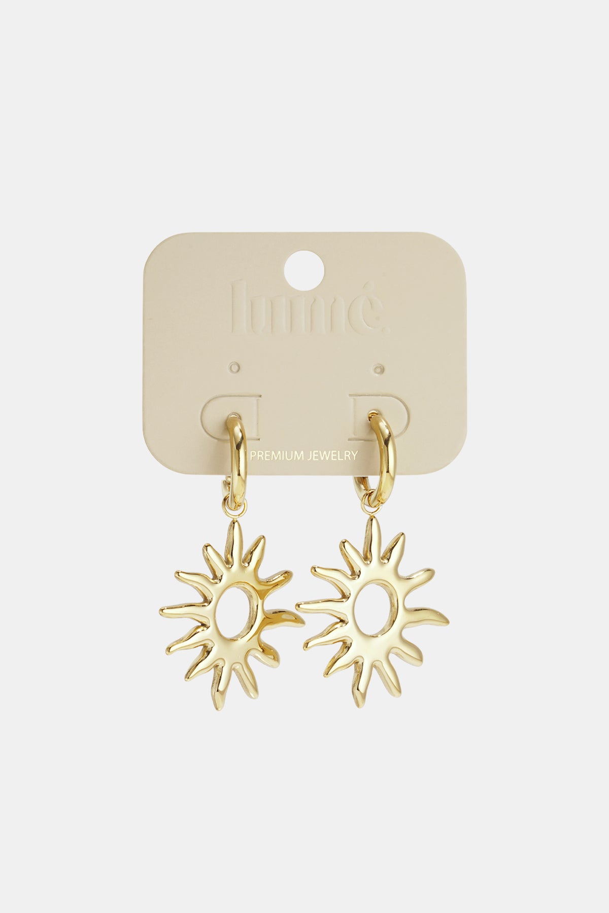 Gold sun drop earrings with pointed rays hanging from gold hoops on a cream backing card.