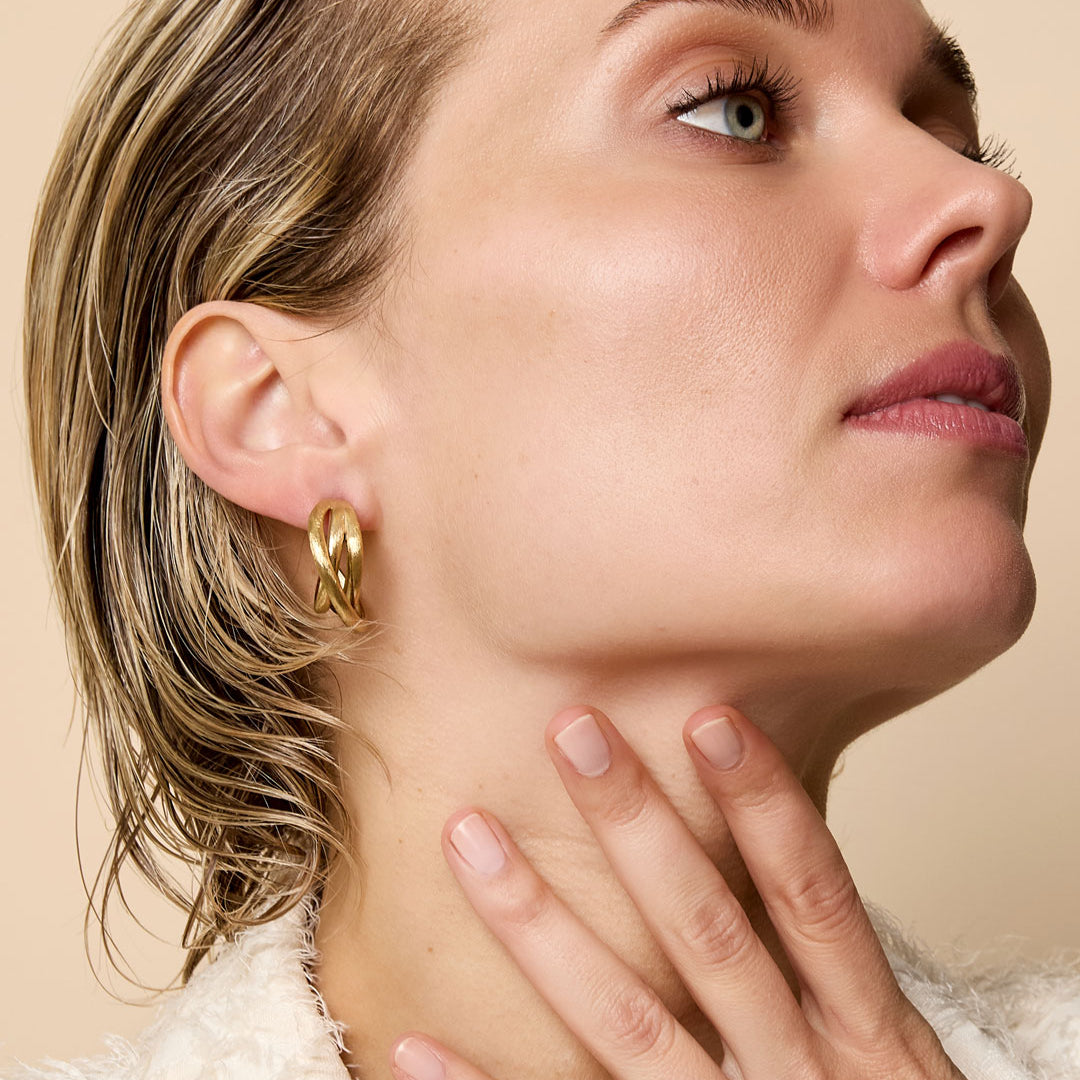 Gold Astra Hoop Earrings on a woman's ear, showcasing their intertwined design.