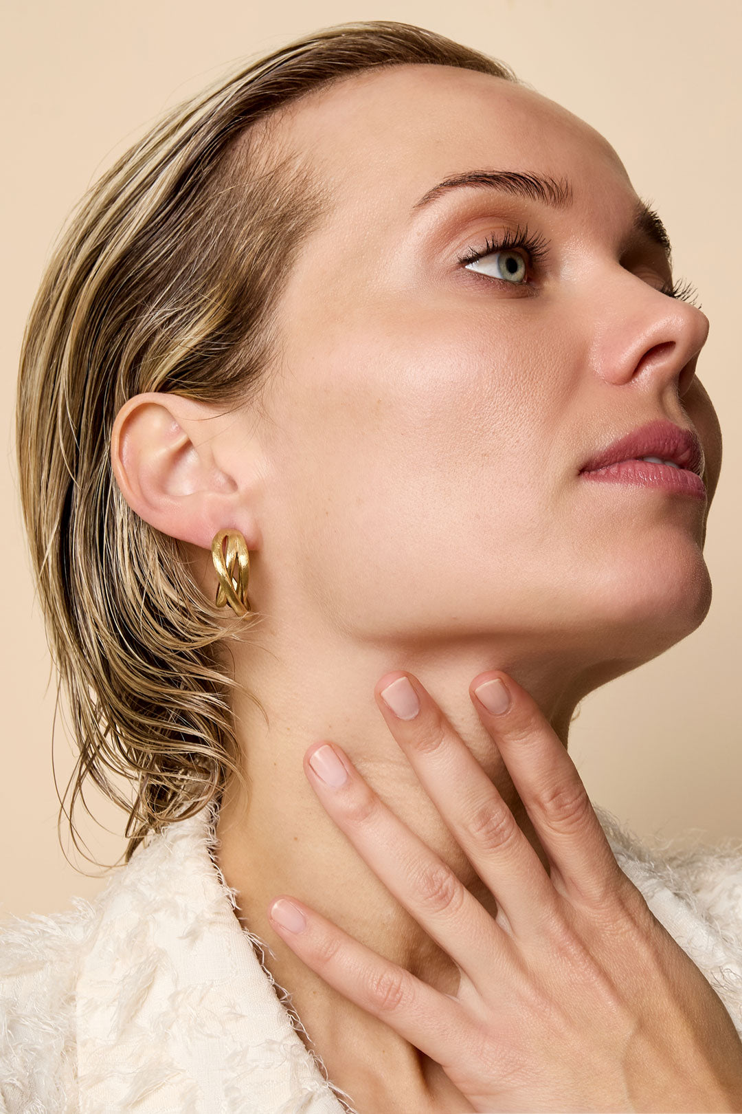 Gold Astra Hoop Earrings on a woman's ear, showcasing their intertwined design.