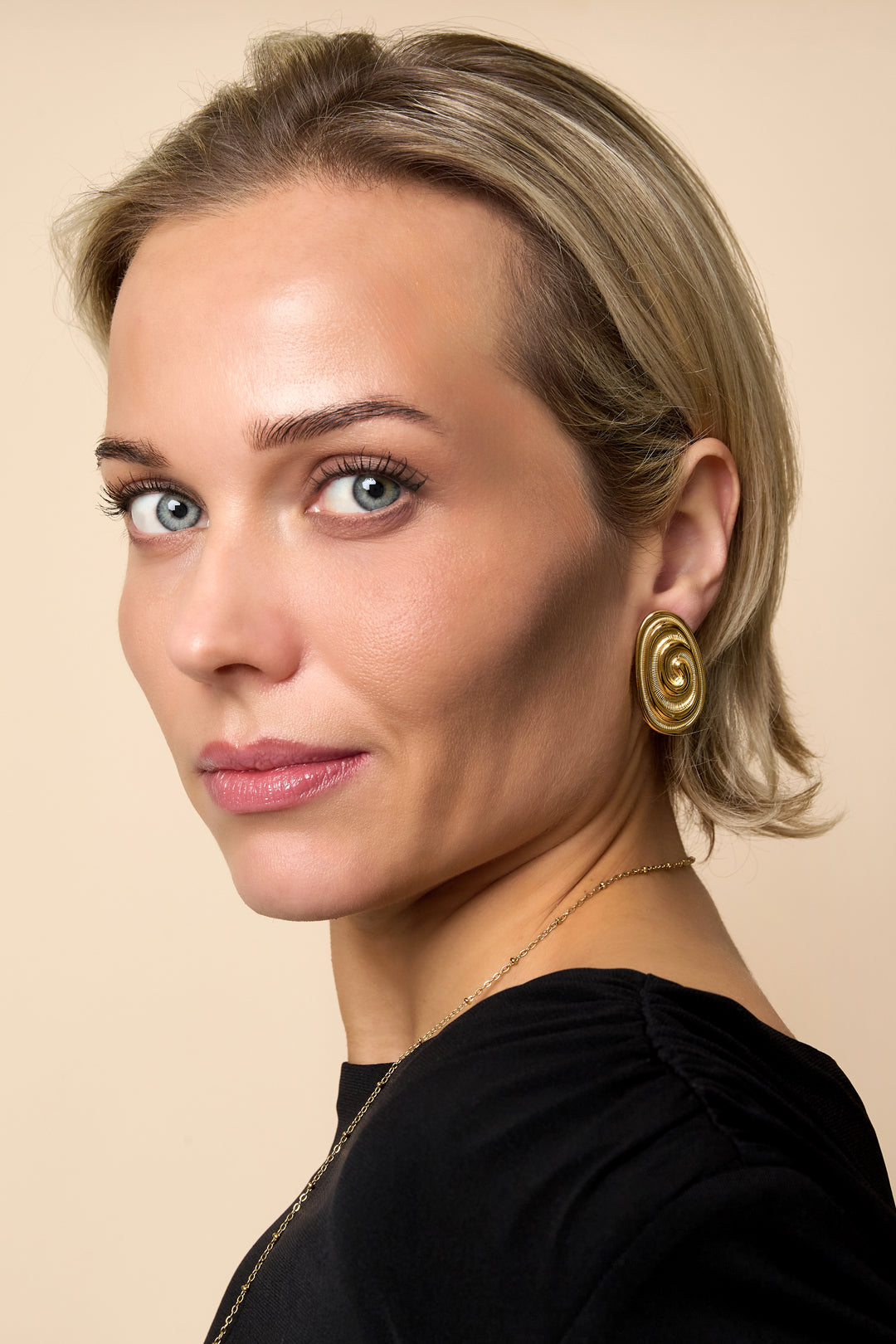 A woman wears irregular gold stud earrings and a gold necklace.