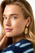 Gold irregular drop earrings with a spiral design, worn by a woman.