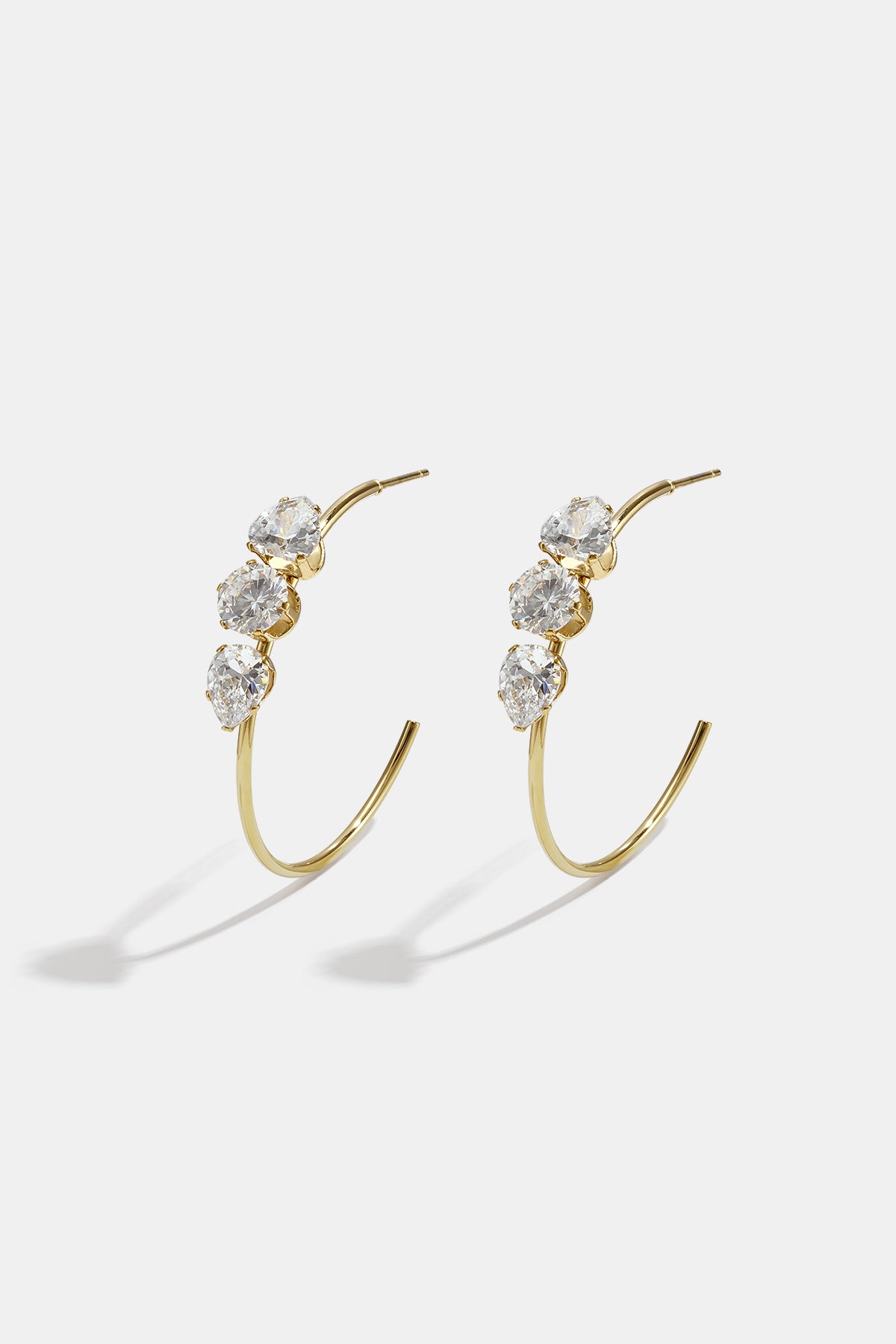 Gold hoop earrings with three clear stones each, on a white background.