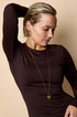 Gold heart pendant necklace on a woman wearing a brown long-sleeved shirt.
